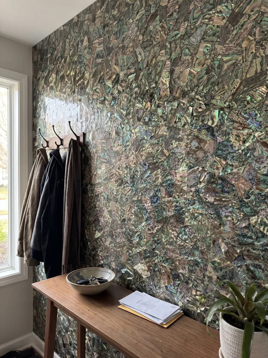 Entryway wall clad in abalone mother of pearl with a narrow console: a tight mosaic of iridescent shell in greens, blues and browns