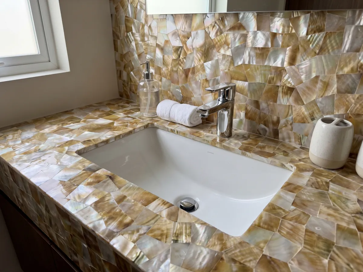 Vanity top and bathroom wall in golden shell mother of pearl with a white sink and chrome fixtures: a mosaic of golden and white mother of pearl with iridescent highlights