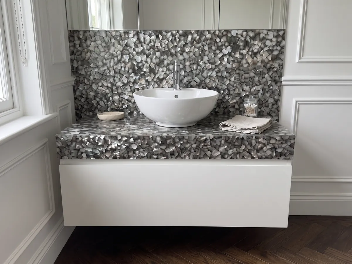 Vanity top and bathroom wall in Gray Shell Mother of Pearl with a white sink and chrome fixtures: polygons of dark gray and silver mother of pearl with iridescent highlights