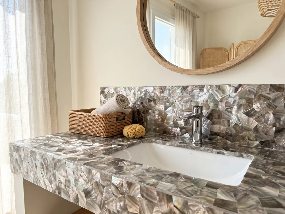 Vanity top and bathroom wall in Brown Shell Mother of Pearl with a white sink and chrome fixtures: pieces of taupe-gray and silvery mother of pearl with an iridescent sheen