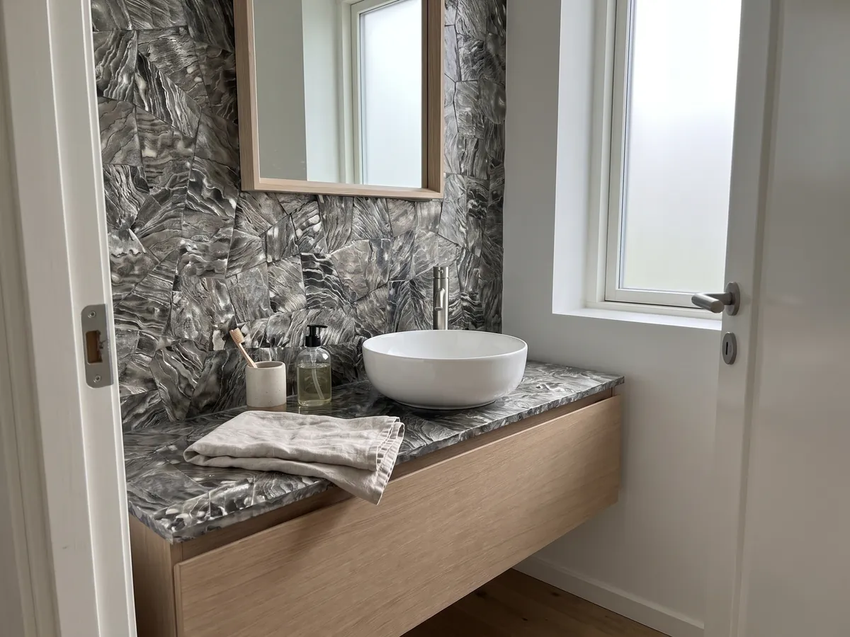 Vanity top and bathroom wall in Galushell Gray Mother of Pearl with a white sink and chrome fixtures: gray-silver shell pieces with wavy, metallic-looking striations