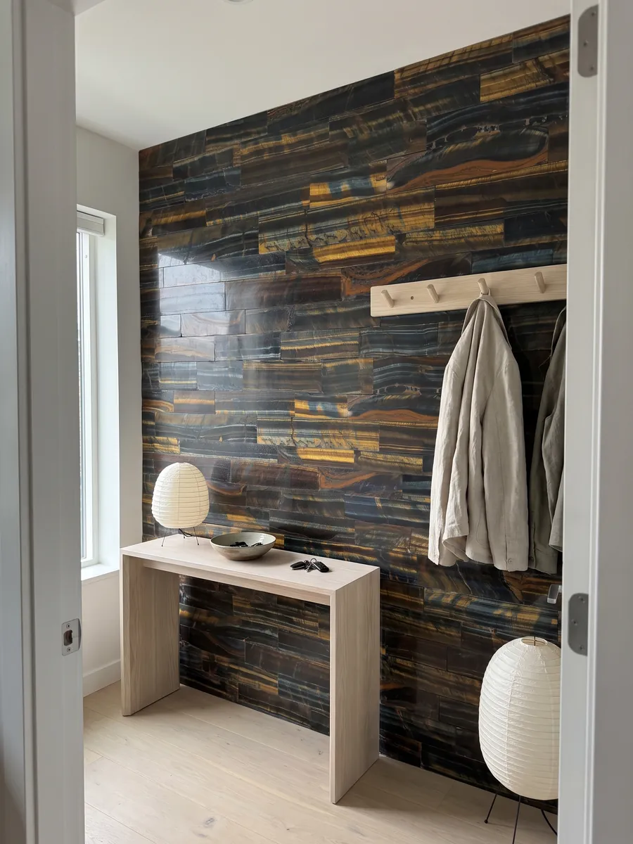 Entryway wall clad in blue and gold tiger's eye with a narrow console: horizontal bands mixing dark blue with golden and orange stripes