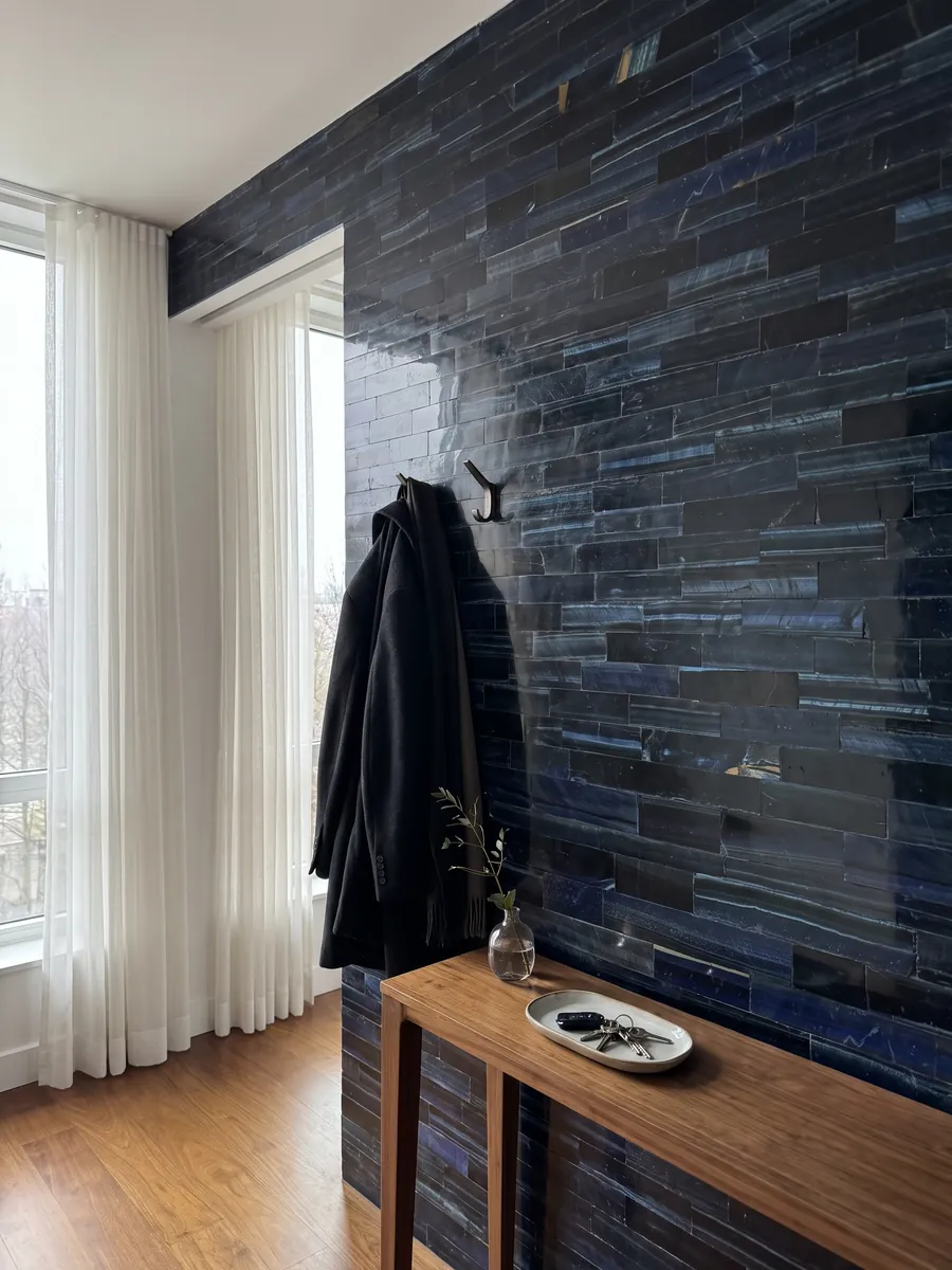 Entryway wall clad in blue tiger's eye with a narrow console: horizontal strips of navy blue, almost black, with blue flashes