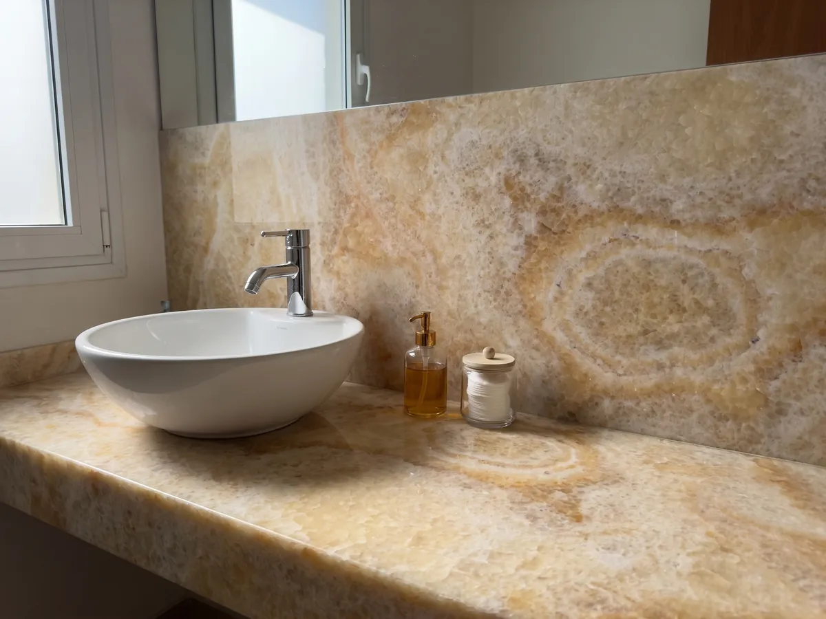 Bathroom vanity top and wall in yellow onyx with a white sink and chrome fixtures: honey and cream with a clearly visible concentric oval ring