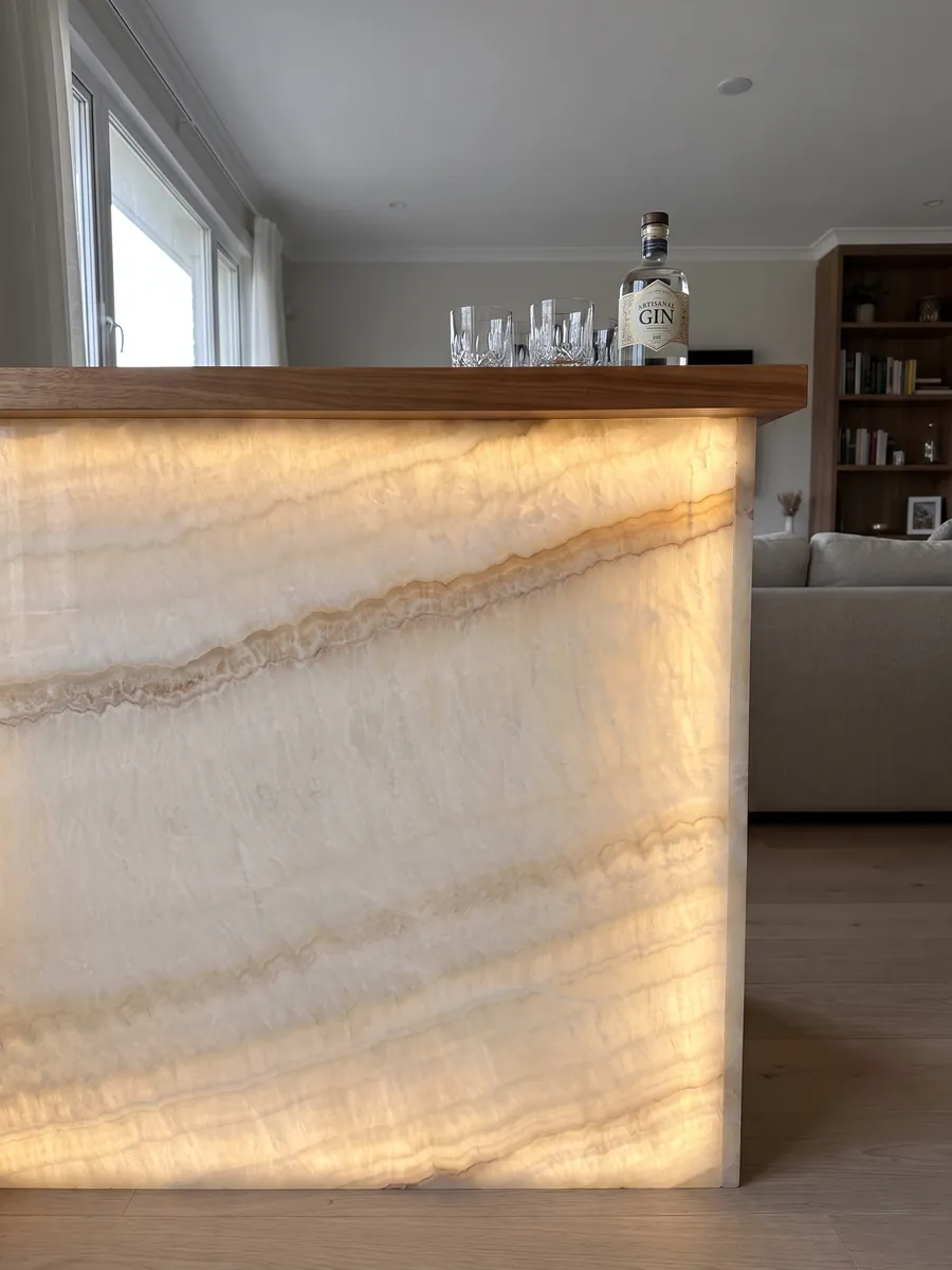 Bar with a backlit front of beige Ivory onyx, the light passing through the stone: soft ivory with faint waves and a fine diagonal honey line