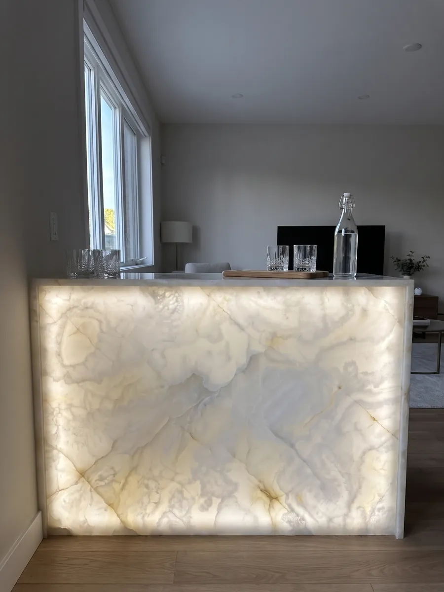 Bar with a backlit white onyx front, the light passing through the stone: translucent creamy white with soft clouds and very fine gold lines