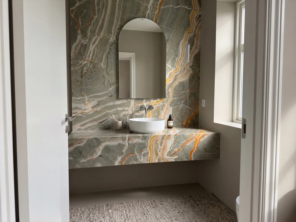 Vanity top and bathroom wall in Rainbow onyx with a white sink and chrome faucets: gray-green crossed by branching orange and yellow veins