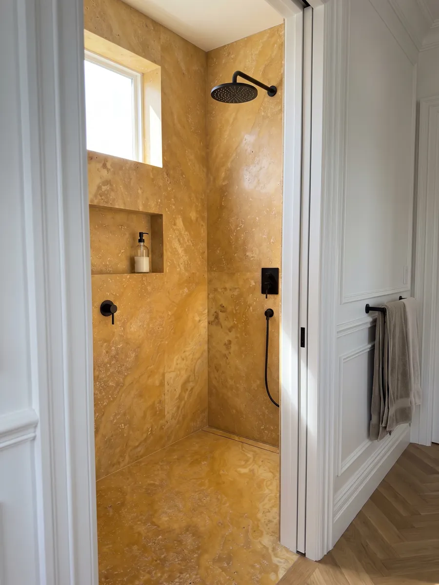 Shower clad in full yellow travertine slabs with a recessed niche: warm golden ochre with small pores and soft clouds of tone