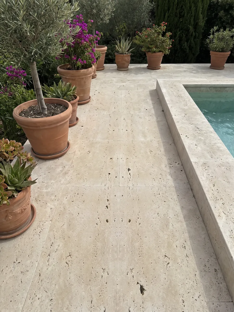 Terrace floor and pool coping in beige Classic travertine with planters: beige with dark holes aligned vertically; the pattern looks symmetrical, as in a mirror