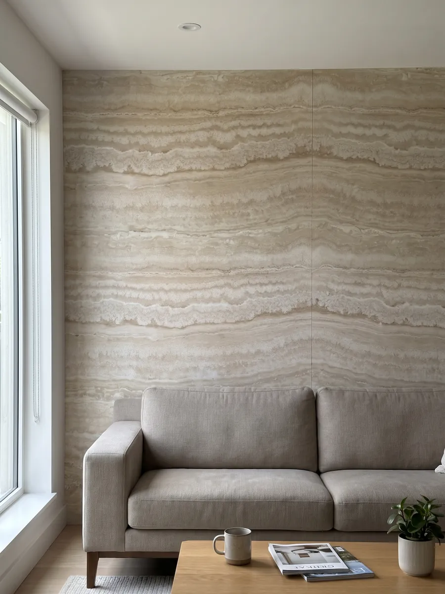 Living room wall clad in bookmatched beige Paglierino travertine slabs behind a sofa: cream with wavy horizontal bands in very close tones