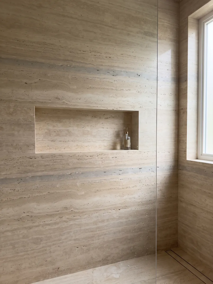 Shower clad in full beige Striato travertine slabs with a recessed niche: beige with fine horizontal stripes and a wider gray band here and there