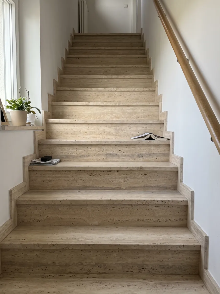 Indoor staircase with beige Striato travertine treads and a handrail: beige with fine horizontal stripes and a wider gray band here and there