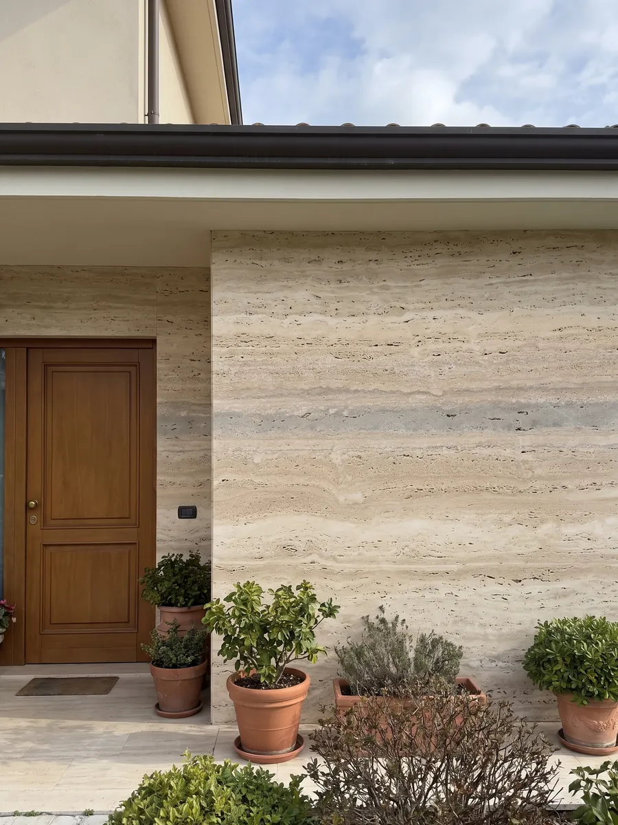 House facade clad in beige Striato travertine next to a wooden door: beige with fine horizontal stripes and a wider gray band here and there