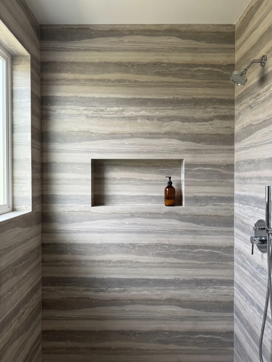 Shower clad in full gray Silver travertine slabs with a recessed niche: wide horizontal bands in gray and light beige, orderly and parallel