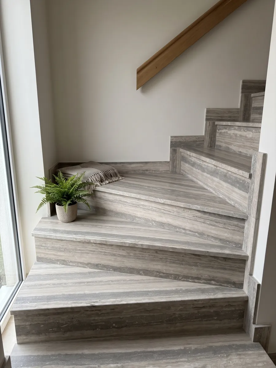 Indoor staircase with gray Silver travertine treads and a handrail: wide horizontal bands in gray and light beige, orderly and parallel