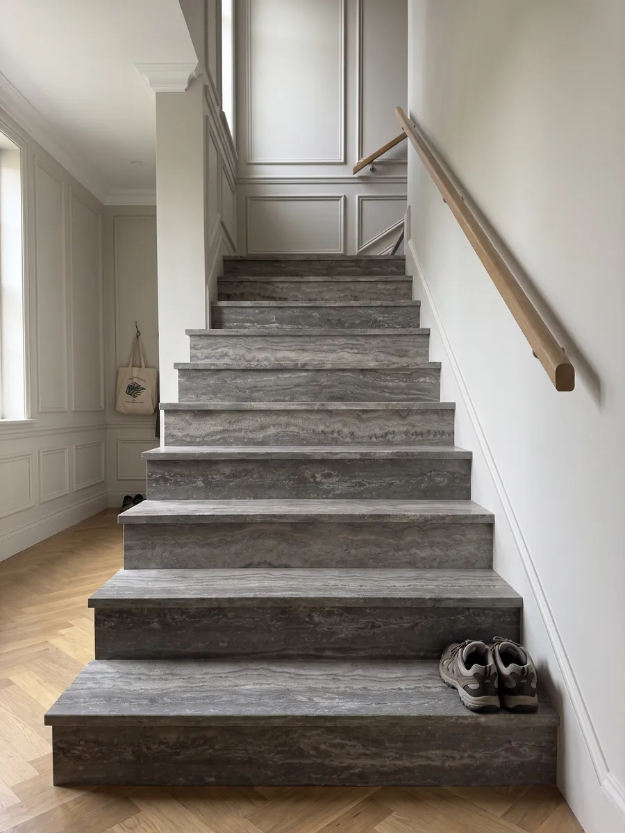 Indoor staircase with gray Titanium travertine treads and a handrail: gray with wavy horizontal bands that move from light to dark