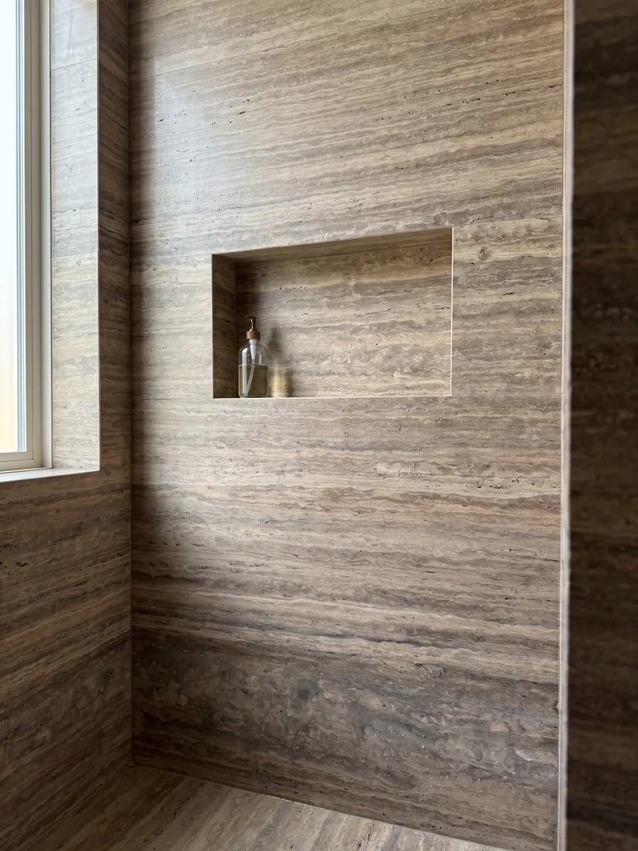 Shower clad in full brown Pantheon travertine slabs with a recessed niche: brown with fine, parallel, lighter horizontal bands