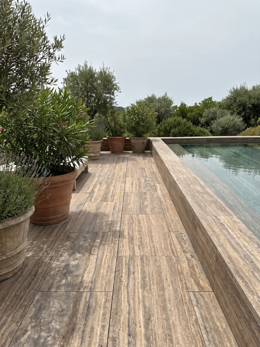Terrace floor and pool coping in brown Pantheon travertine with planters: brown with fine, parallel, lighter horizontal bands