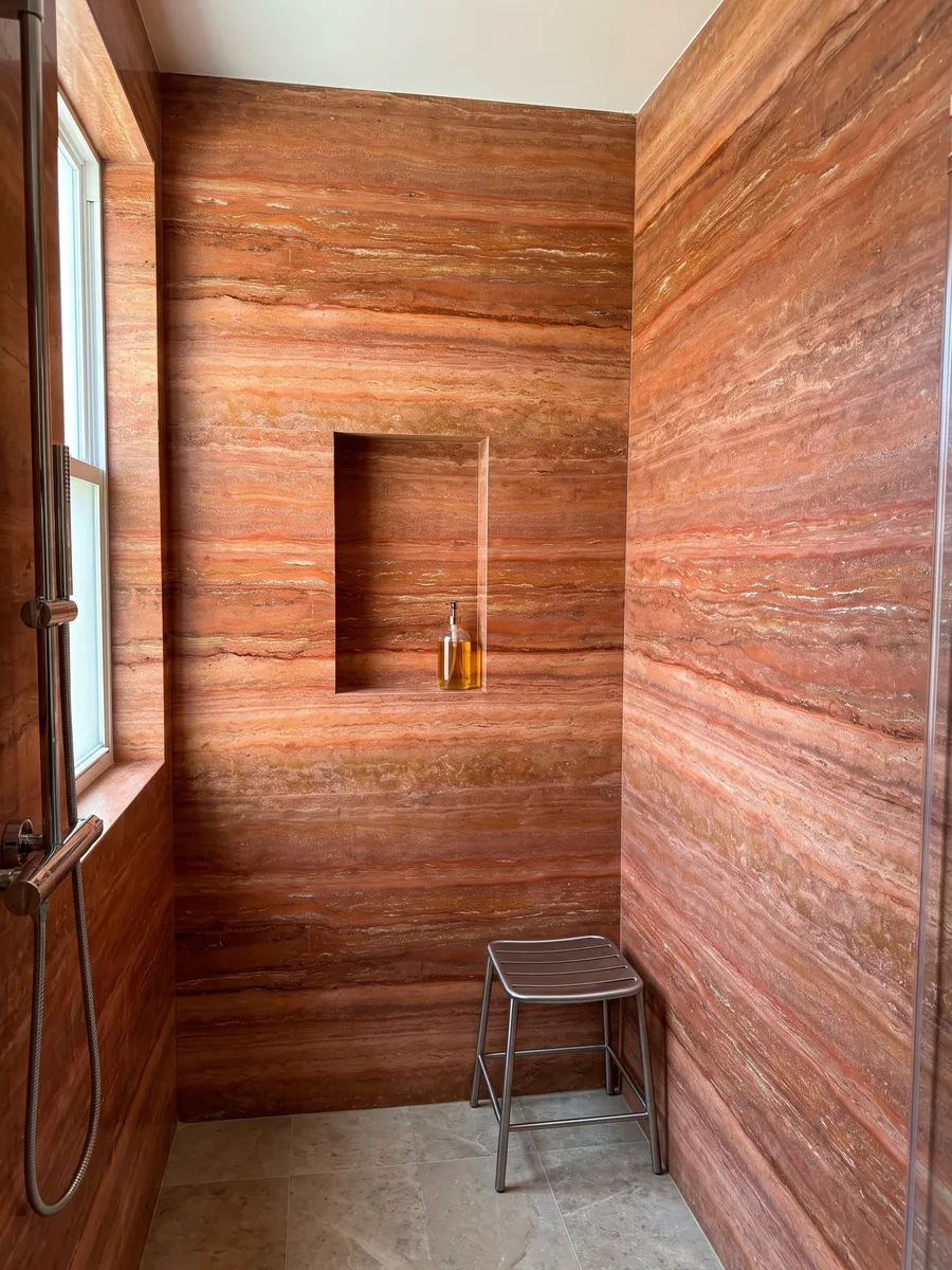 Shower clad in full red travertine slabs with a recessed niche: intense orange-red in horizontal bands with fine cream lines