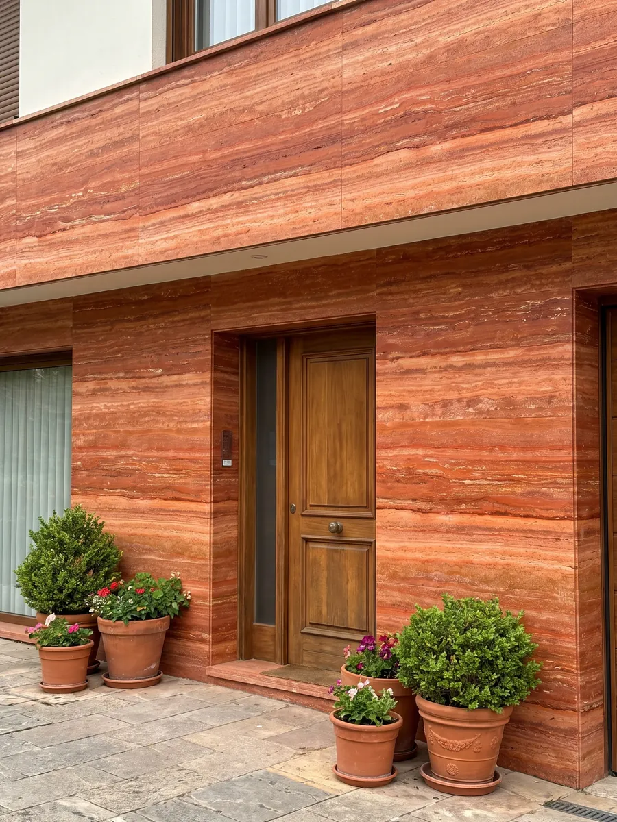 House facade clad in red travertine next to a wood door: intense orange-red in horizontal bands with fine cream lines