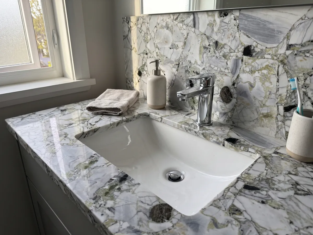 Vanity top and bathroom wall in White Beauty with a white sink and chrome fittings: white and gray fragments joined by light green areas, with loose black pieces