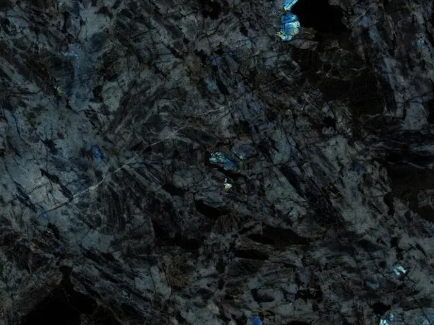 Close-up of Lemurian black quartzite: dark elongated crystals and electric blue flashes on the polished surface