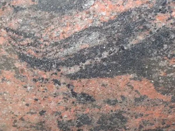 Slab of Indian Aurora Granite: wavy bands of coral, gray and black running diagonally over a dark gray background