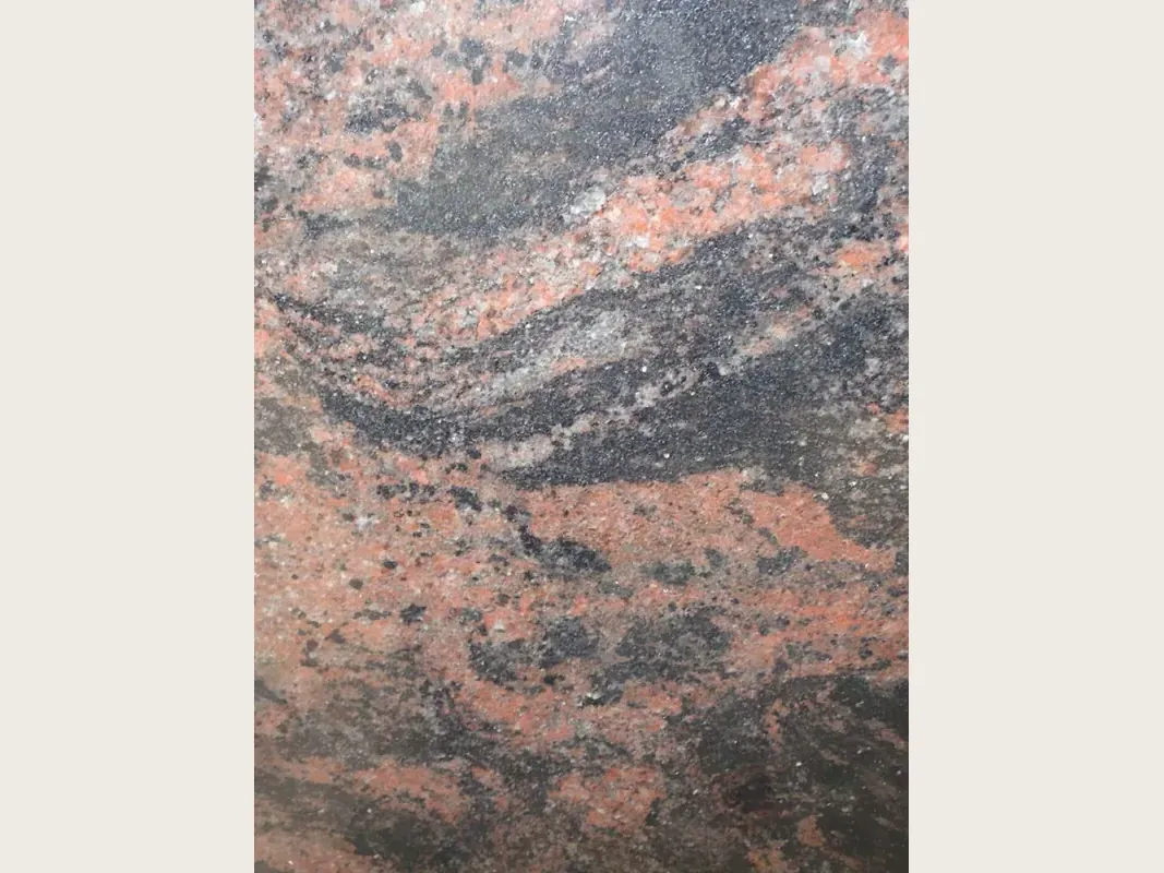 Slab of Indian Aurora red granite: wavy coral, gray and black bands running diagonally over a dark gray background