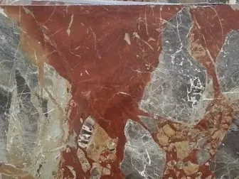 Close-up of gray Macchia Vecchia marble: a rust-red patch with greenish gray fragments and the sheen of the polish