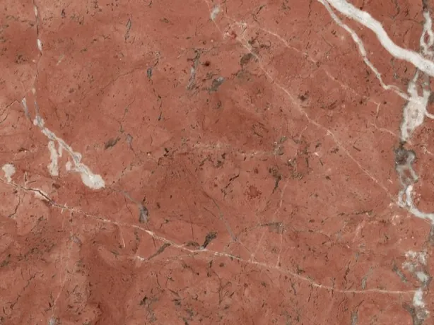 Close-up of Rojo Alicante marble: a diagonal white vein and dark flecks over the polished red