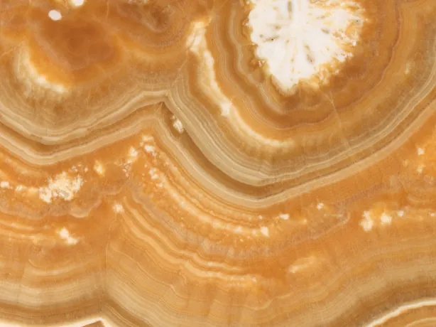 Detail of the orange Arancio onyx: the curve of orange, amber and cream bands with the gloss of the polish