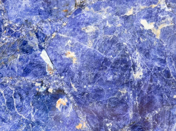 Sodalite detail: irregular white veins and small orange flecks over the violet blue