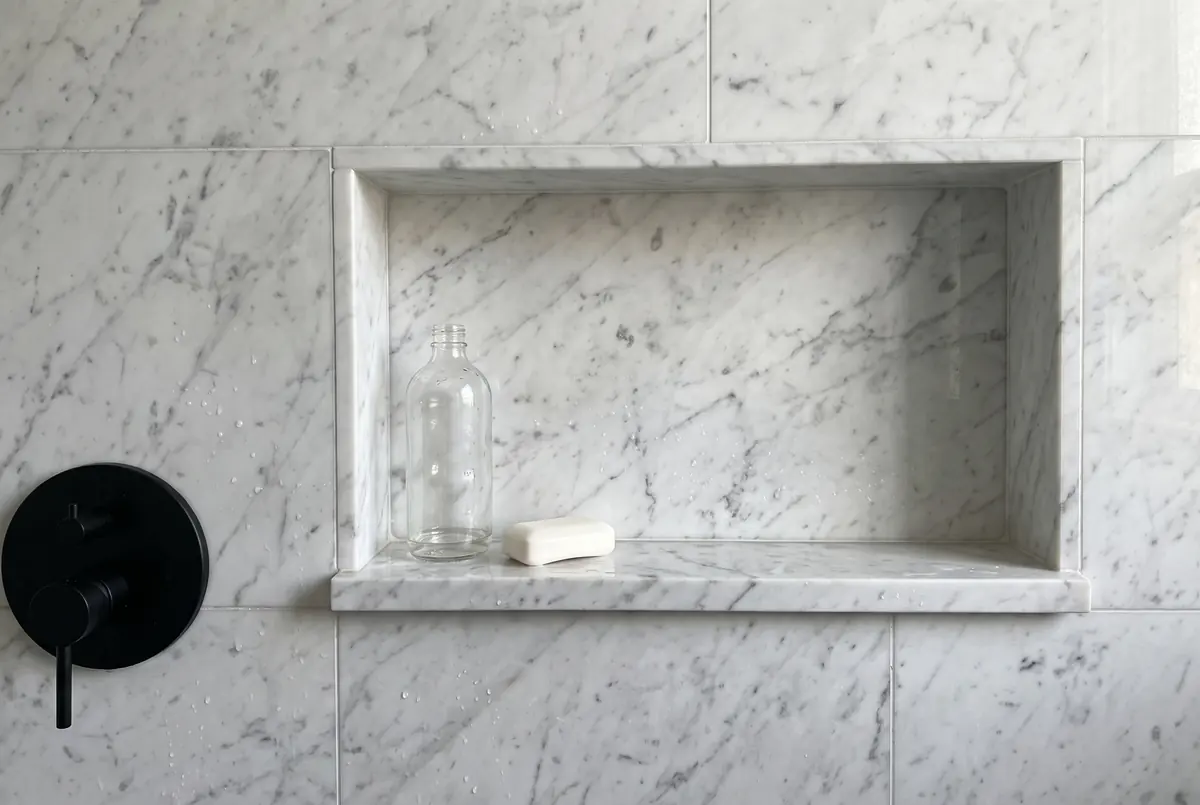 Shower niche clad in Carrara marble with a shelf of the same stone