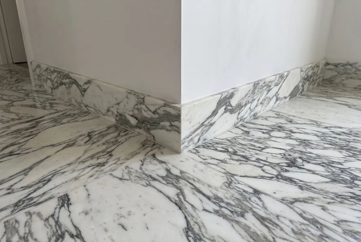 Arabescato marble baseboard at the corner of a wall, over a floor of the same stone