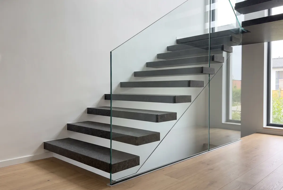 Staircase with floating dark gray granite treads and a glass railing